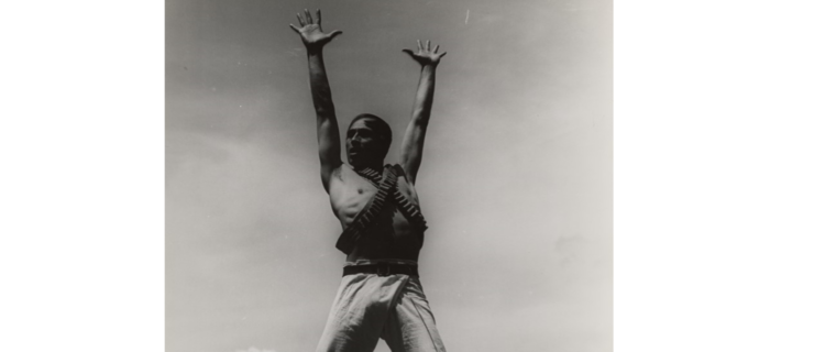 a male dancer standing on an outdoor stage lifting his arms over his head