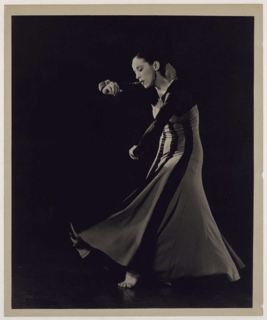 a female dancer wearing a long dress contracting over with arms in front