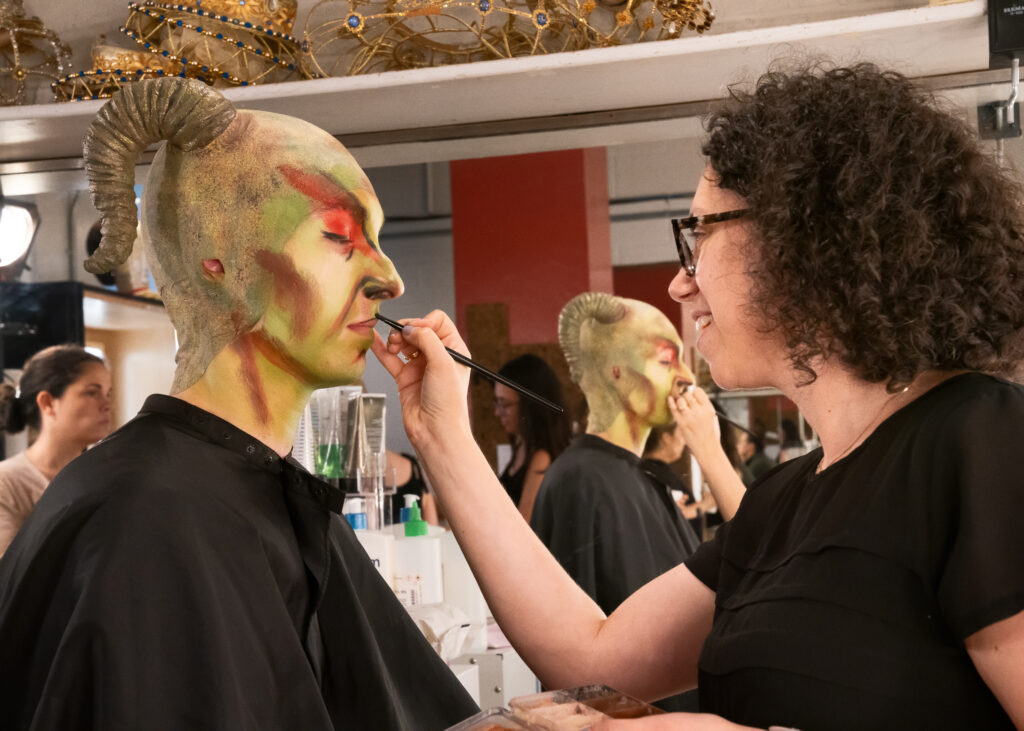a woman helping a dancer with dramatic stage makeup 