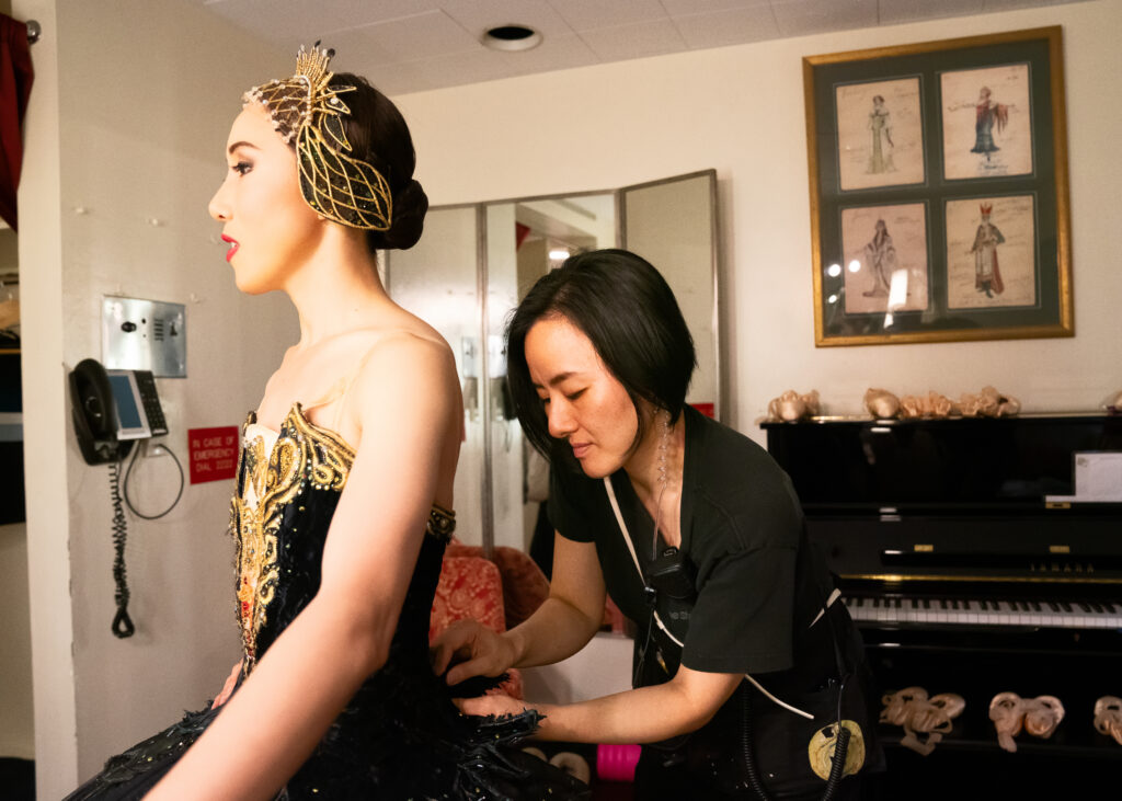 a woman helping a female dancer change into a black tutu