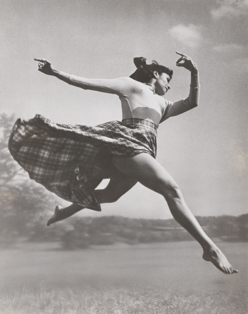 a female dancer mid air leaping in a field wearing a long skirt
