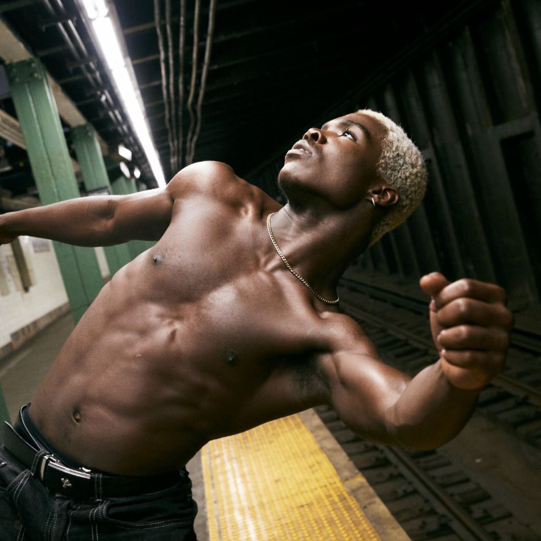 a shirtless male dancer leaning backwards on a subway platform