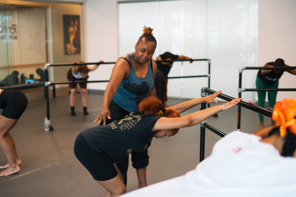 a female teacher instructing students at the barre