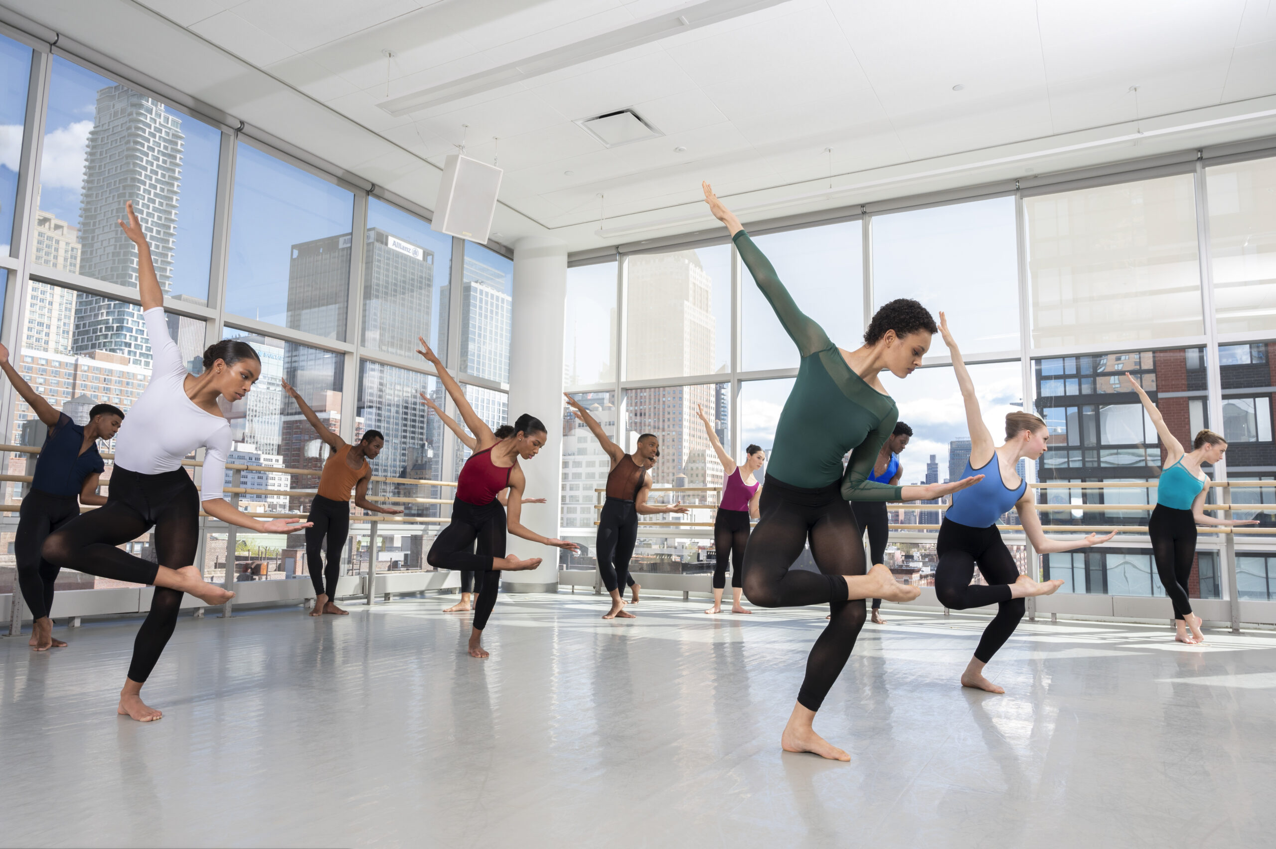 a large group of dancers in a studio with big windows, all posed with leg crossed and lateral bend