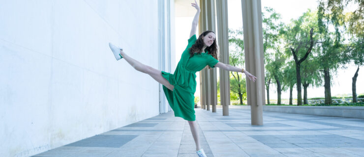 a female dancer wearing a green dress and sneakers extending her leg in a la seconde