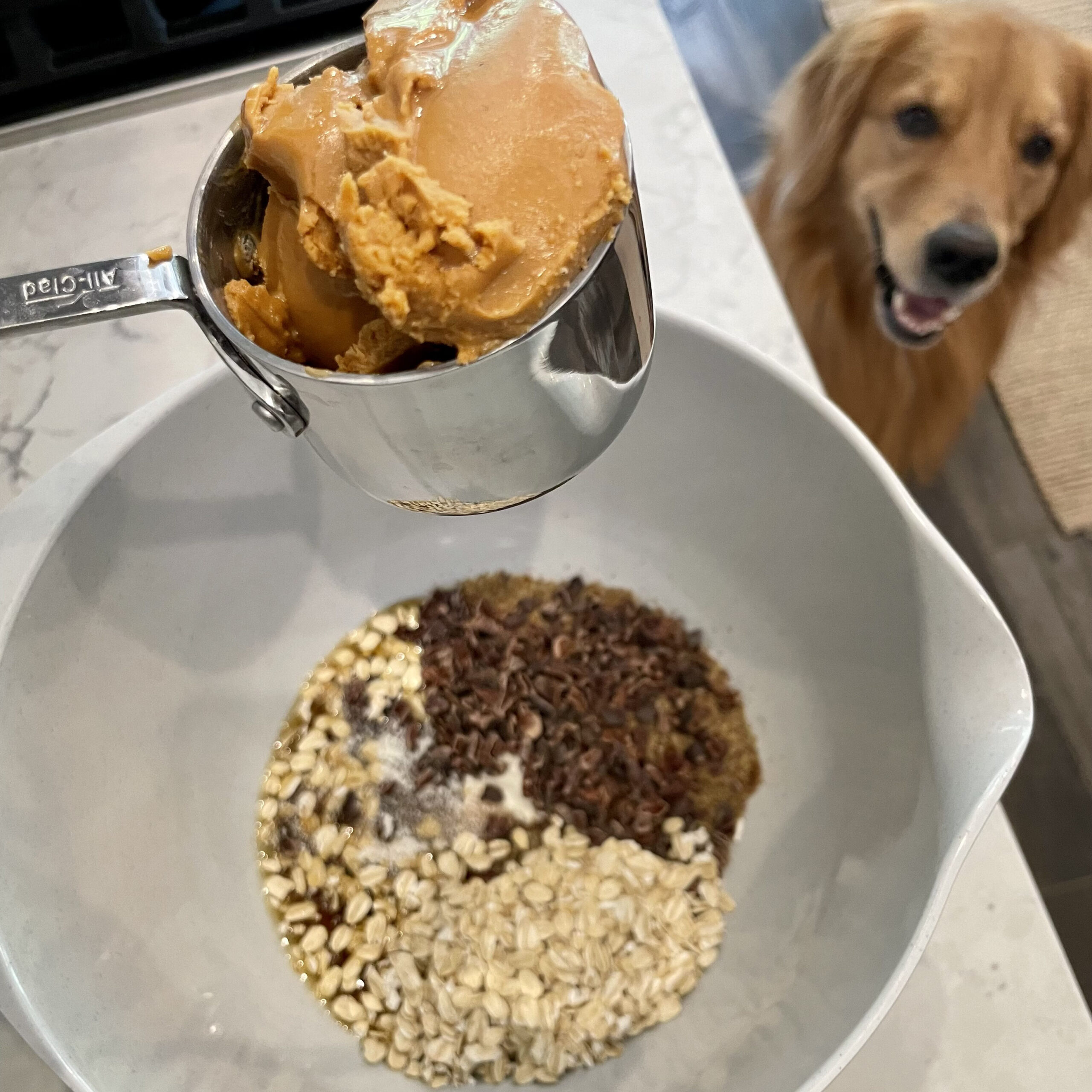 a bowl with ingredients, a cup with peanut butter, and a dog in the background 