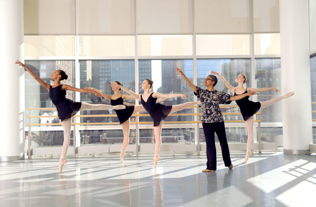 a teacher leading a group of female dancer performing an arabesque 