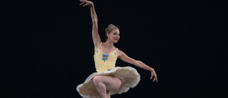 a female dancer wearing a yellow tutu performing a parallel passe en pointe