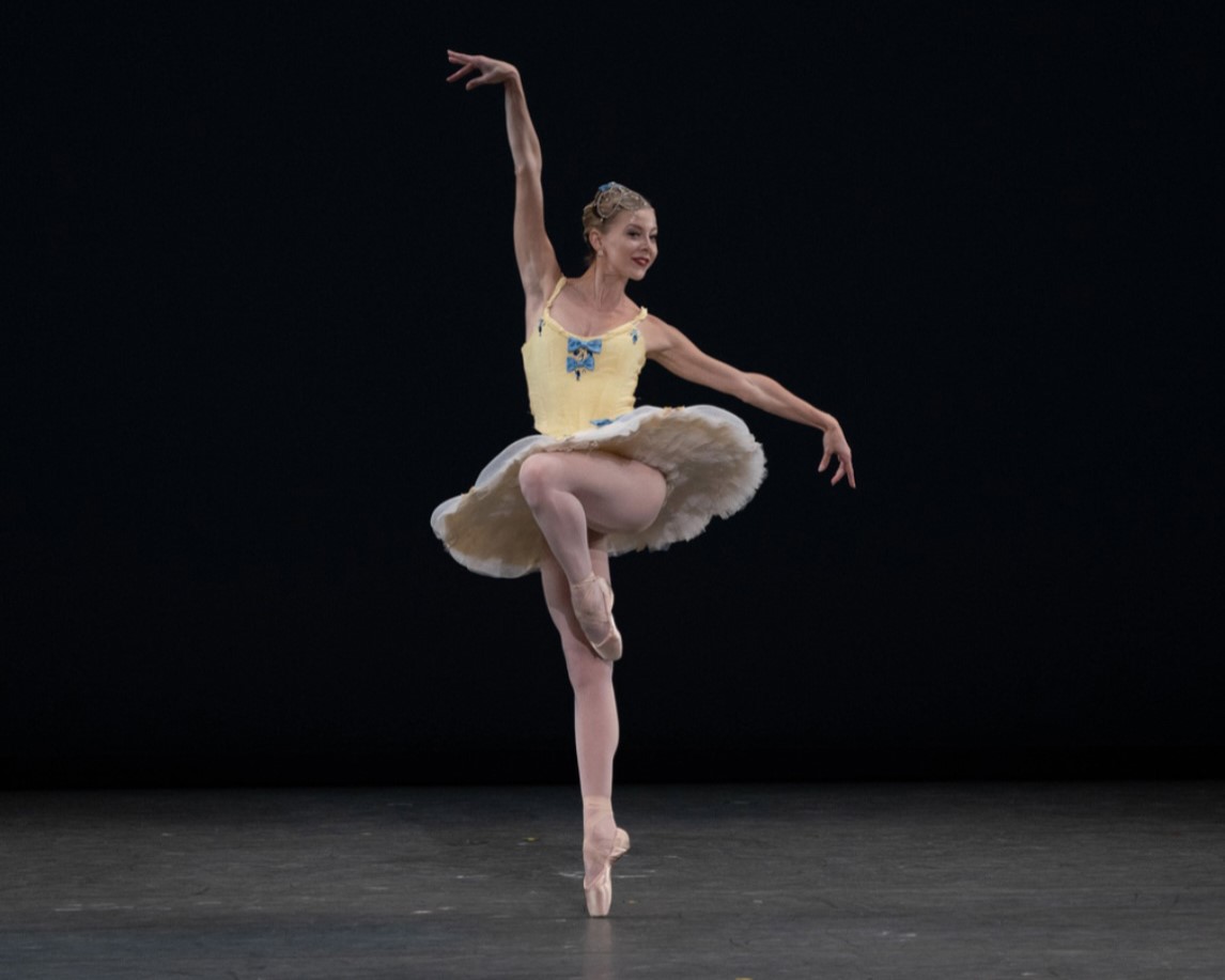 a female dancer wearing a yellow tutu performing a parallel passe en pointe
