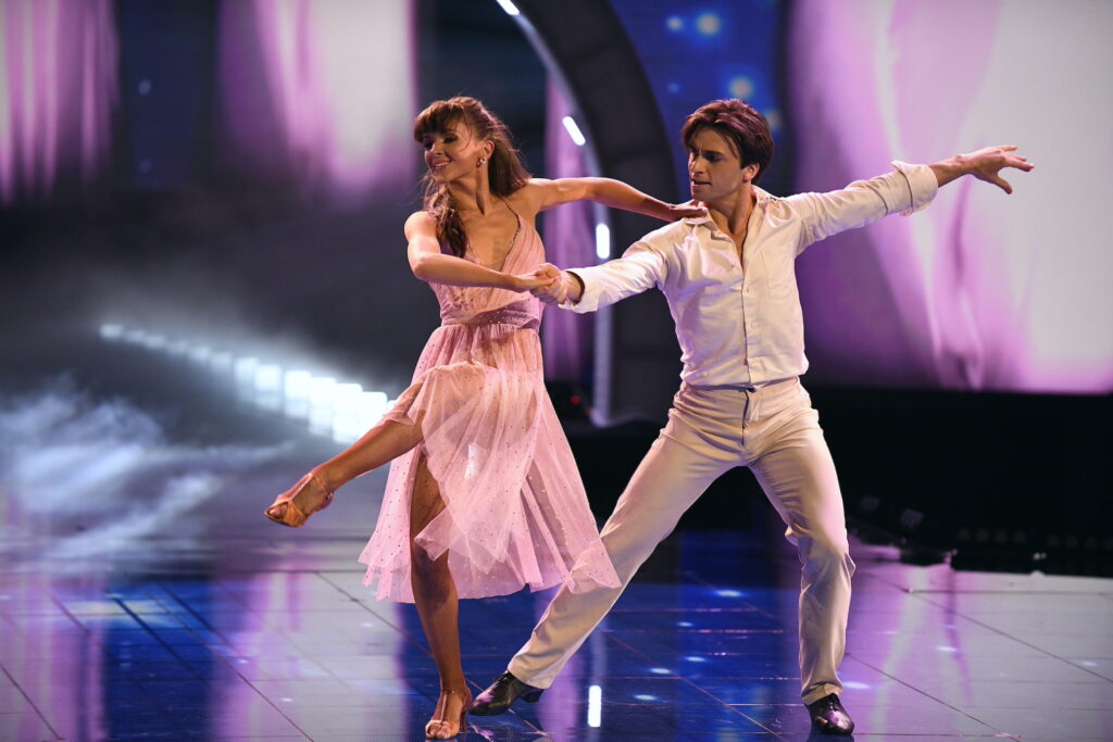 a male and female dancer partnering on stage with pink lights 