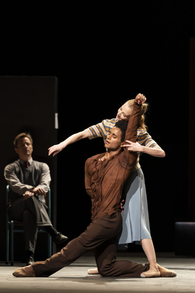 a man dressed in brown kneeling with a female dancer standing directly behind him