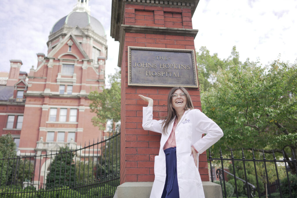 a woman wearing a lab coat standing next to a pillar that says "The Johns Hopkins Hospital" 