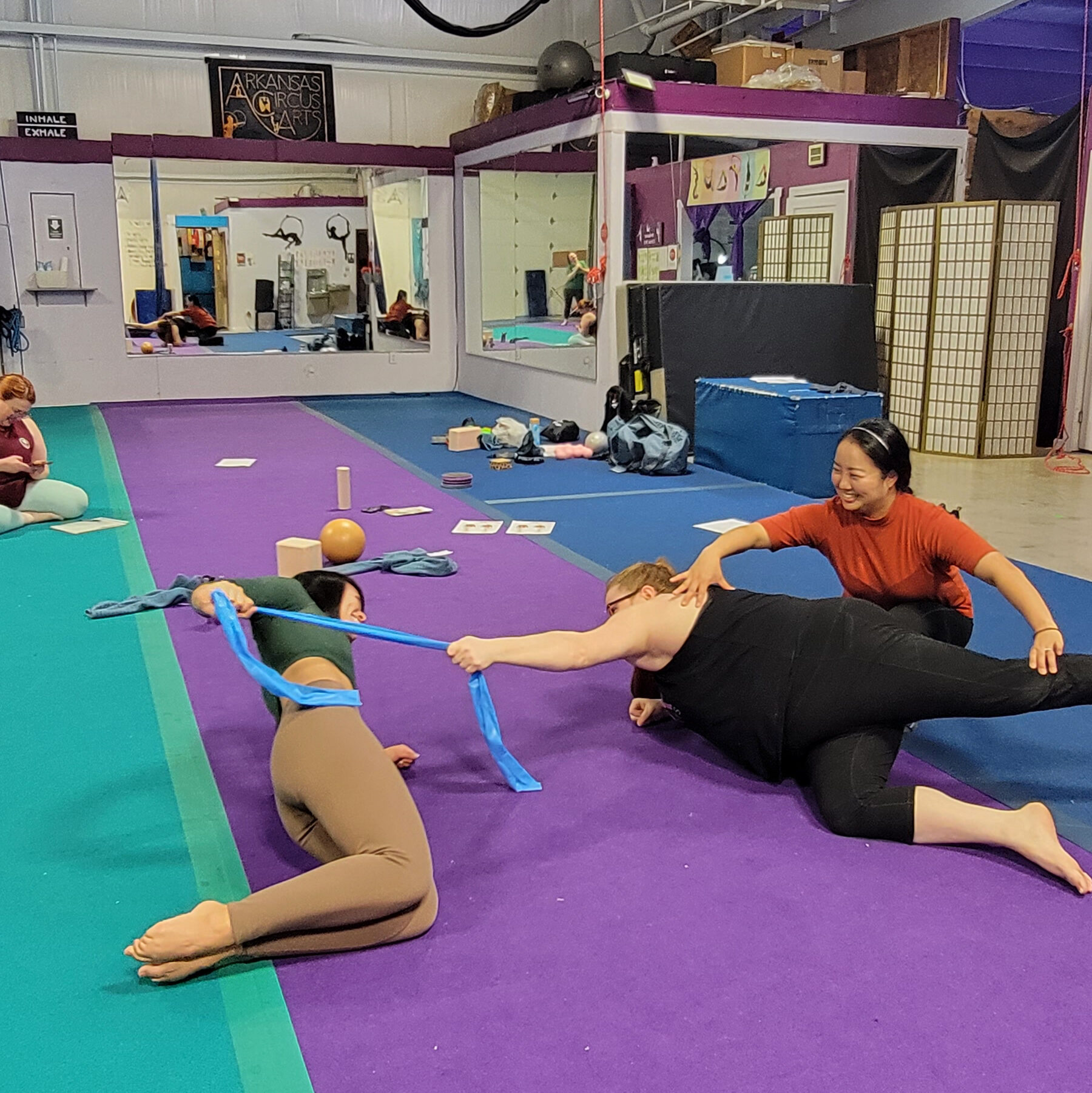 3 dancers on the floor performing an exercise with a resistance band 