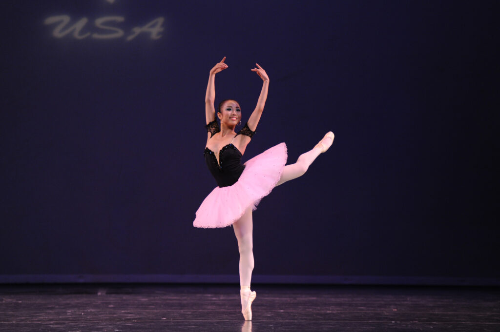 O dansatoare într-o fustă de balet roz execută o atitudine târzie pe scenă 