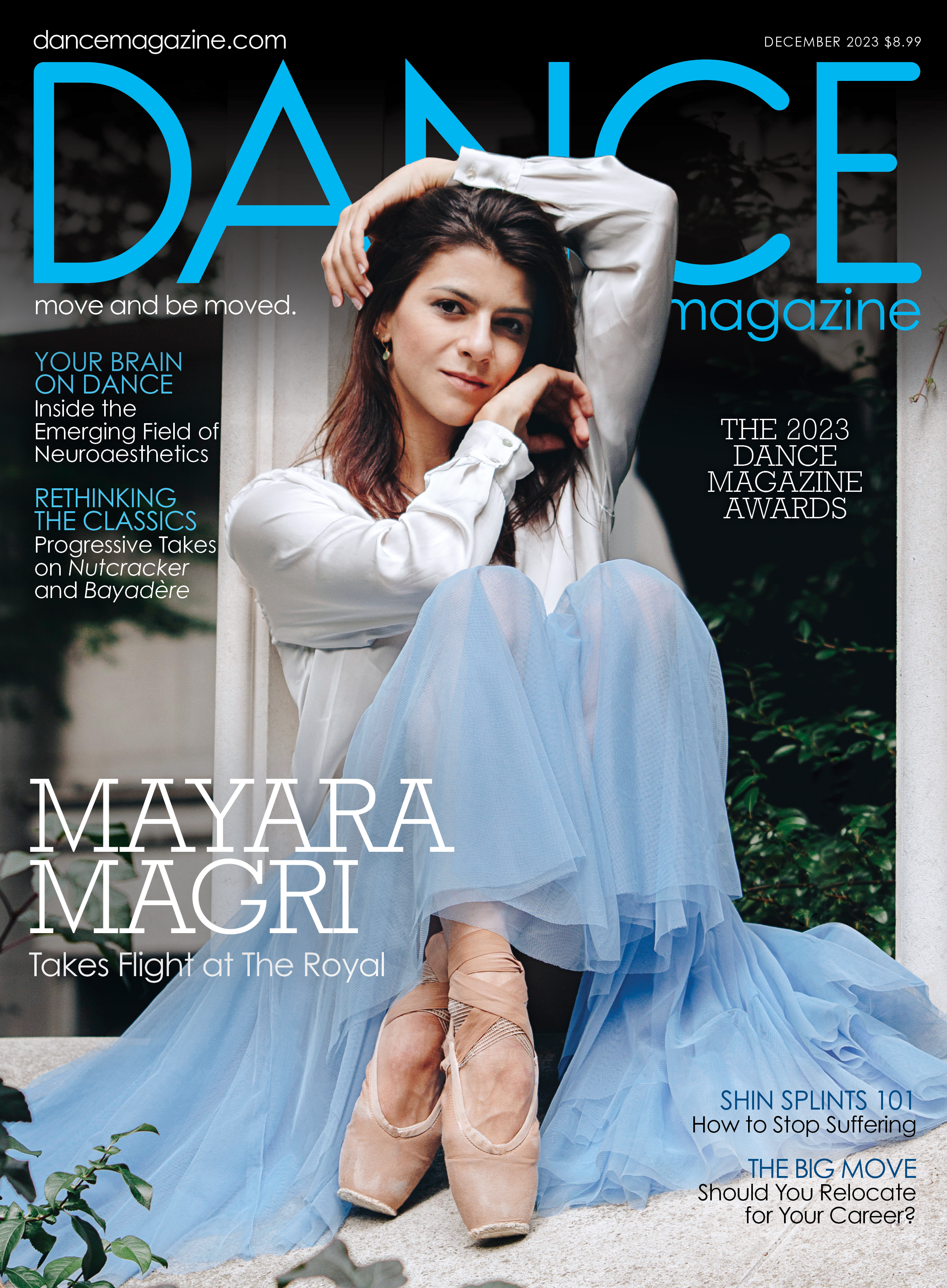 The cover of the December 2023 issue of Dance Magazine. Mayara Magri sits against a window, drawing her knees up to her chest as her hands frame her face. Her brown hair is loose to her shoulders; she wears a long sleeved white blouse, a blue romantic tutu, and pointe shoes. The largest cover line reads, "Mayara Magri Takes Flight at the Royal."