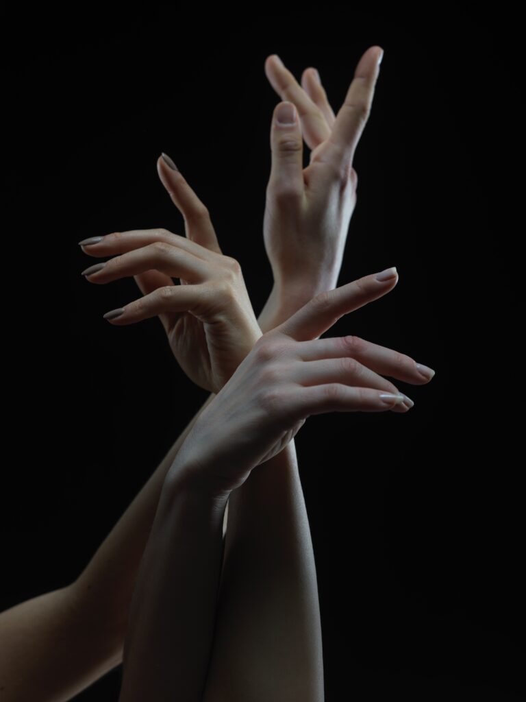 Three hands intertwine gracefully against a black backdrop.