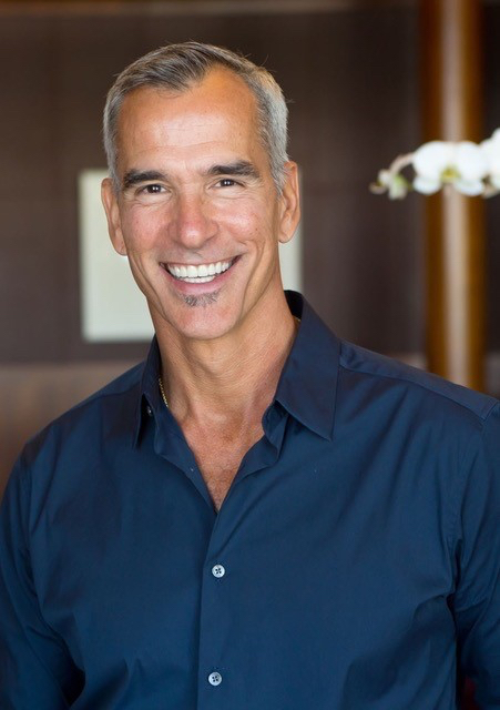Mitchell, a man with salt-and-pepper hair wearing a navy button-down shirt, smiles broadly.