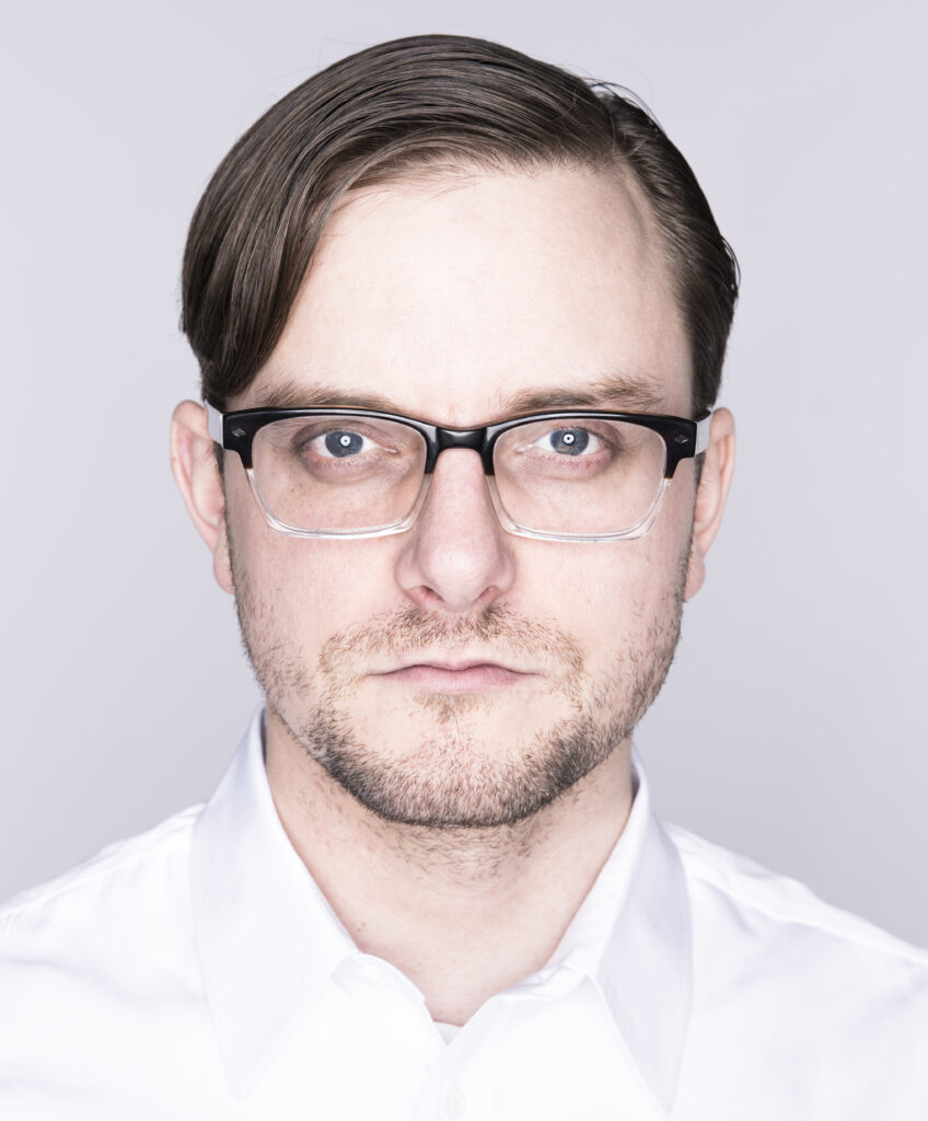 Skybetter, a fair-skinned man wearing a white button-down and glasses, looks directly into the camera.