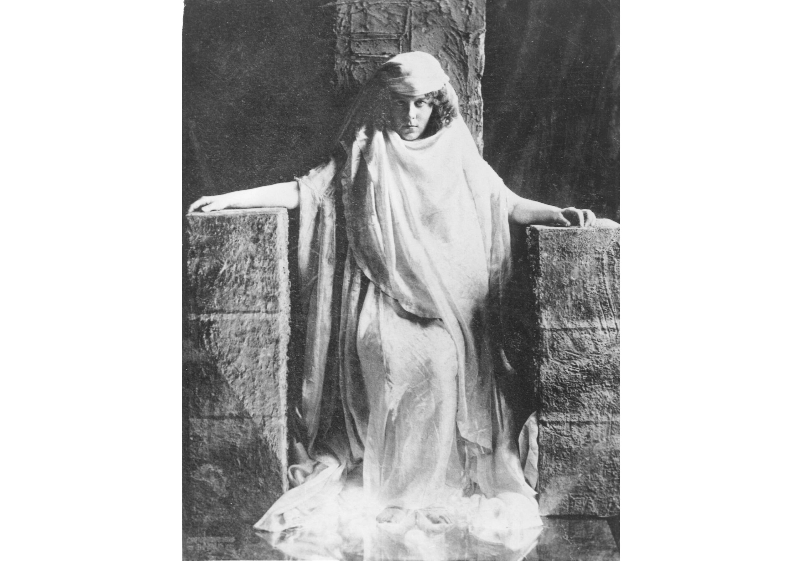 Fuller, wearing a flowing garment and headdress, sits regally on a stone throne.