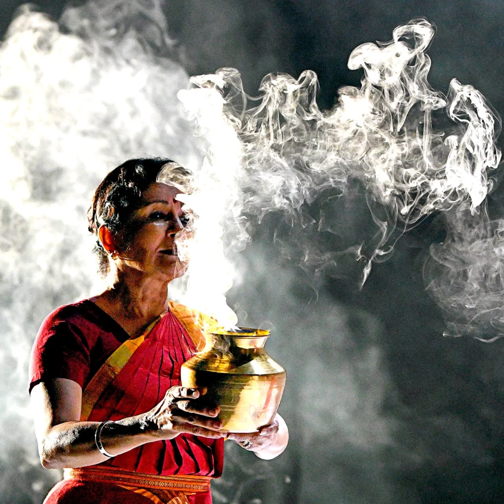 Ranee Ramaswamy holds a golden vessel from which the smoke of burning incense plumes.