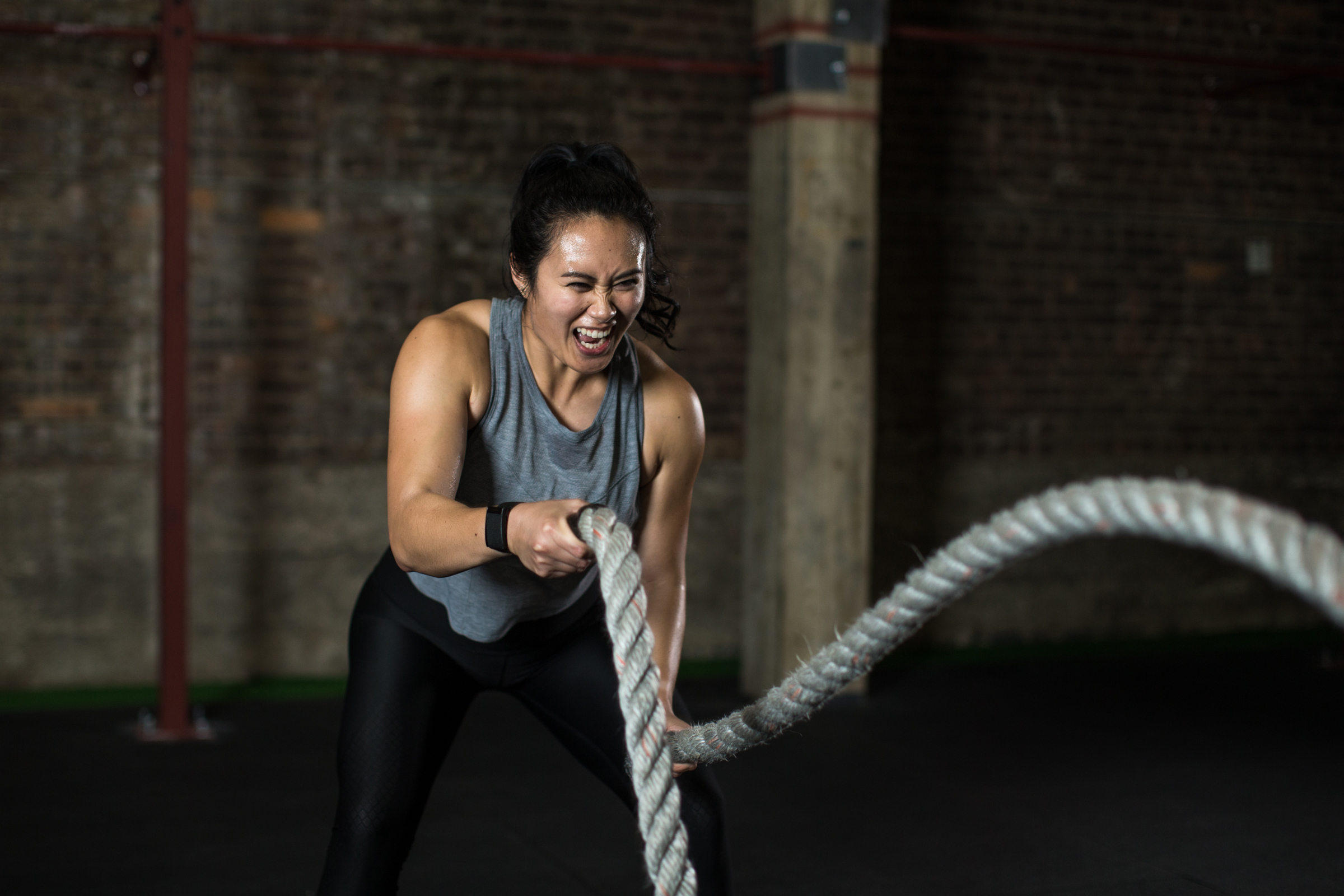a woman in a grey tank top swinging ropes in both hands