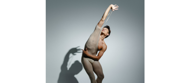 a male dancer wearing a sheet unitard stretching the arm band up over his head