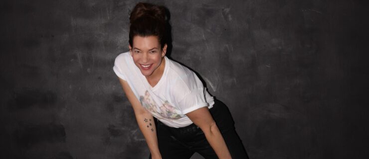 a woman wearing a white tshirt and black pants lunging side and smiling at the camera