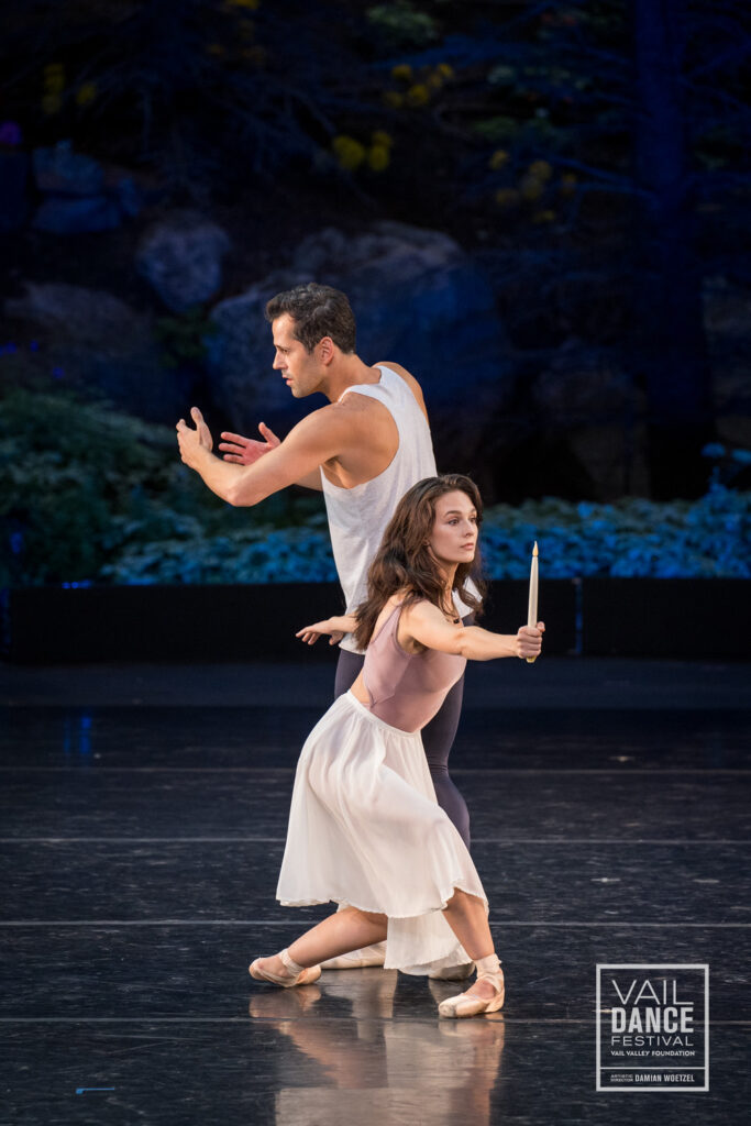 a male and female dancer on stage, the female is holding a candle while lunging in front of the male