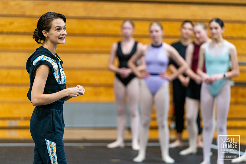 a female instructor addressing a group of dancers in class