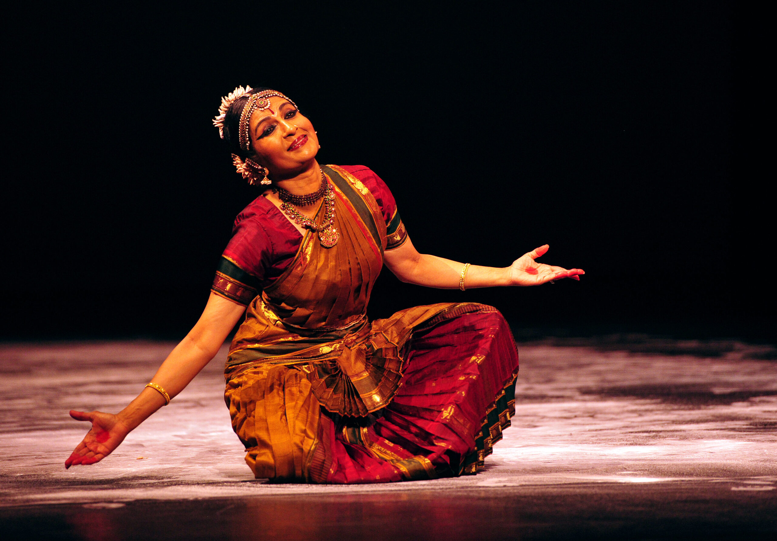 a woman wearing traditional Indian clothing sitting on the floor of a stage