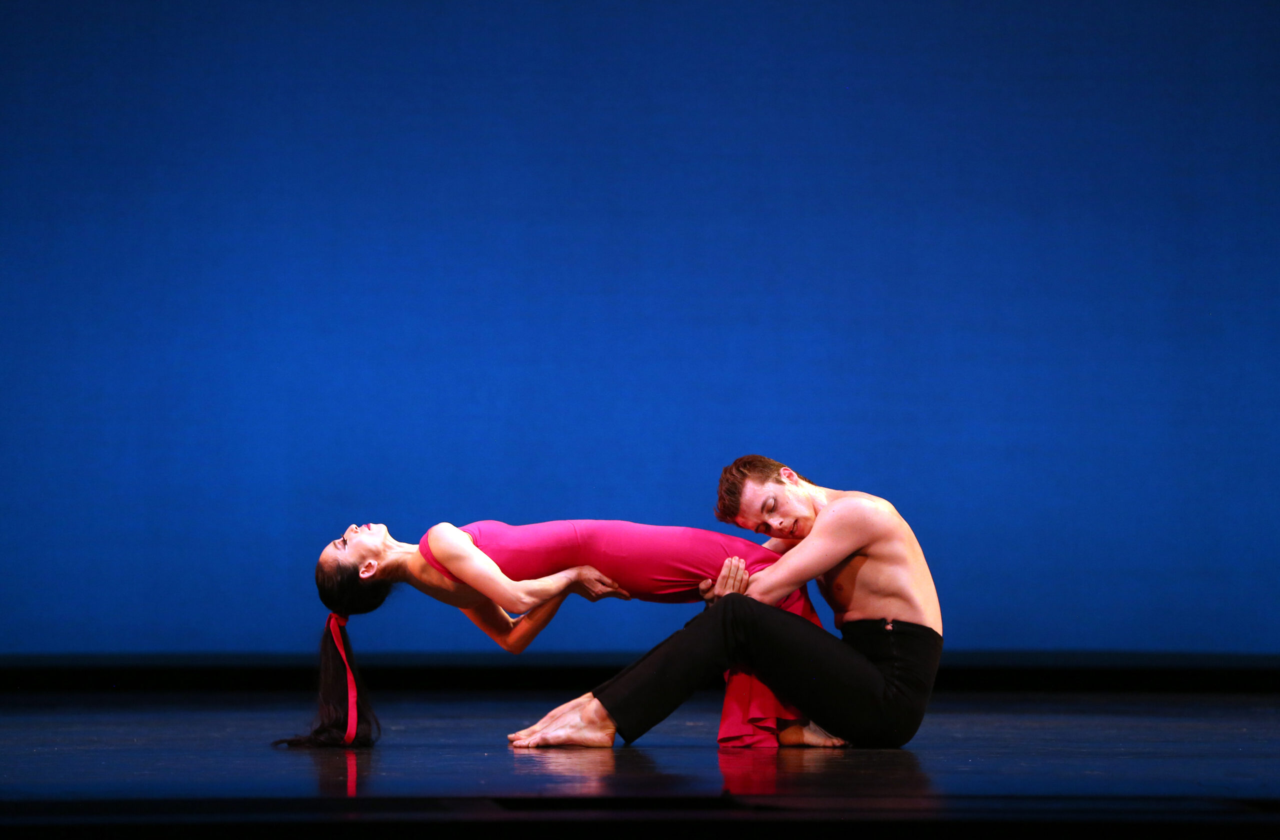 a man sitting on the stage floor holding a woman by the knees as she hinges back