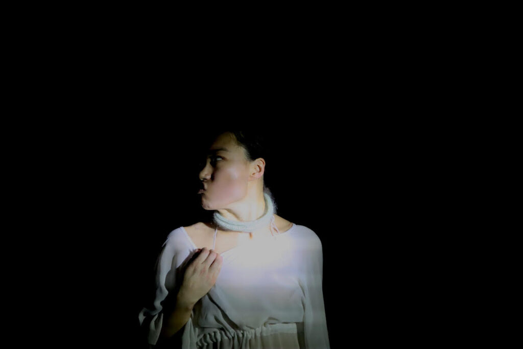 a dark photo with a woman wearing white center. she is looking to the right 