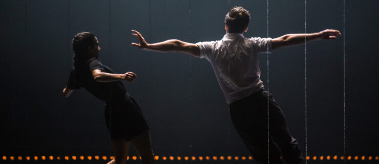 Two dancers face upstage, leaning off balance to their left. One outstretches their arms straight side, pulling toward their left hip. To their left, a dancer facing them rocks onto their back foot, shoulders up as they avoid the other dancer's extended hand.