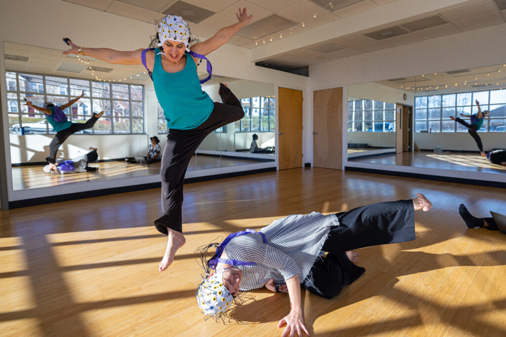 two women dancing in a studio, both wearing tight caps with wires attached
