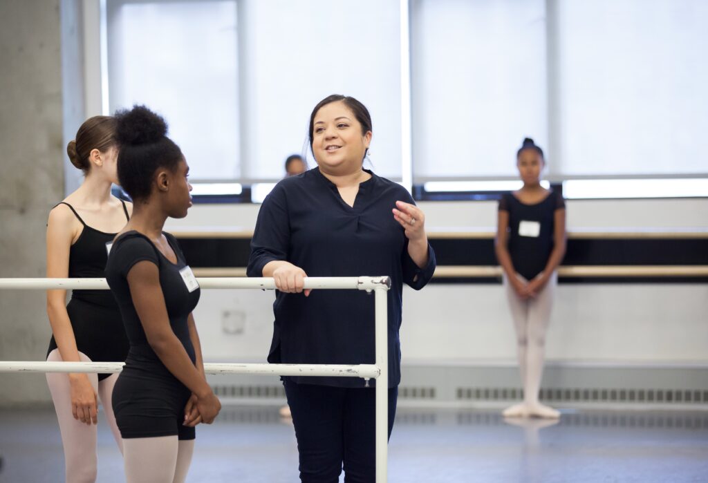 a female instructor addressing students at the barre