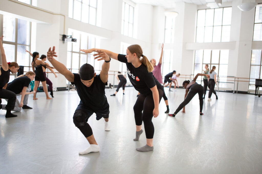 a group of students dancing in a large studio with windows all along the walls