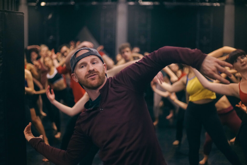 a male teacher leading a large group of dancers behind him 