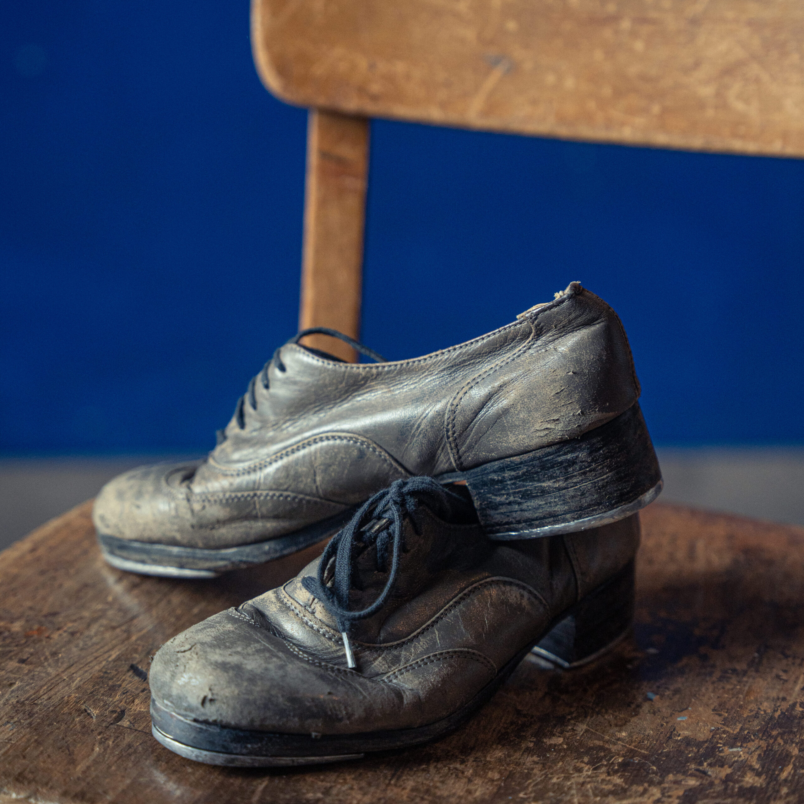 a pair of worn, broken-in tap shoes sitting on a wooden chair 