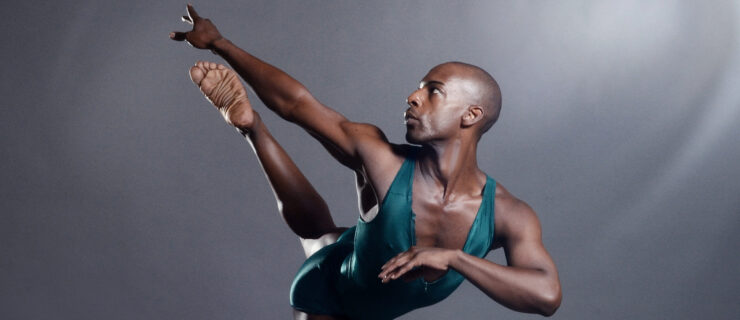 a male dancer wearing a teal unitard posing against a grey backdrop