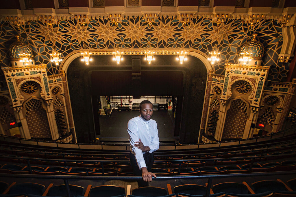 a male wearing a button down shirt standing in the balcony of a theater