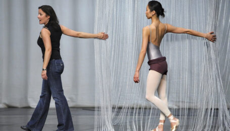 a female choreographer wearing jeans and a black tank top teaching a dancer in a studio