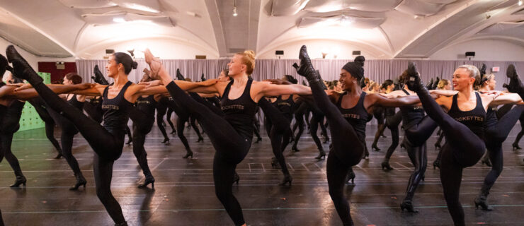 a large group of dancers performing a kickline in rehearsal