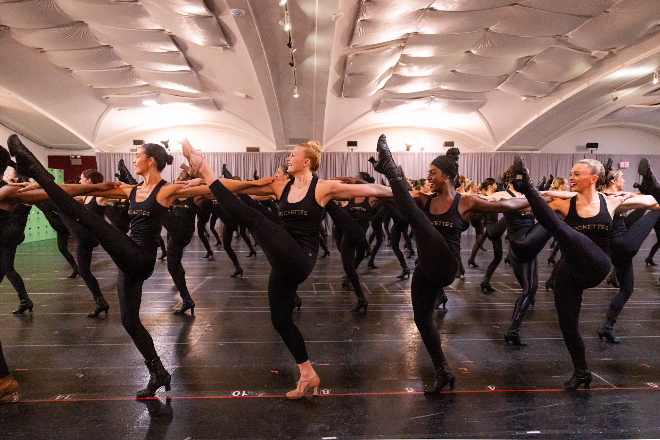 a large group of dancers performing a kickline in rehearsal