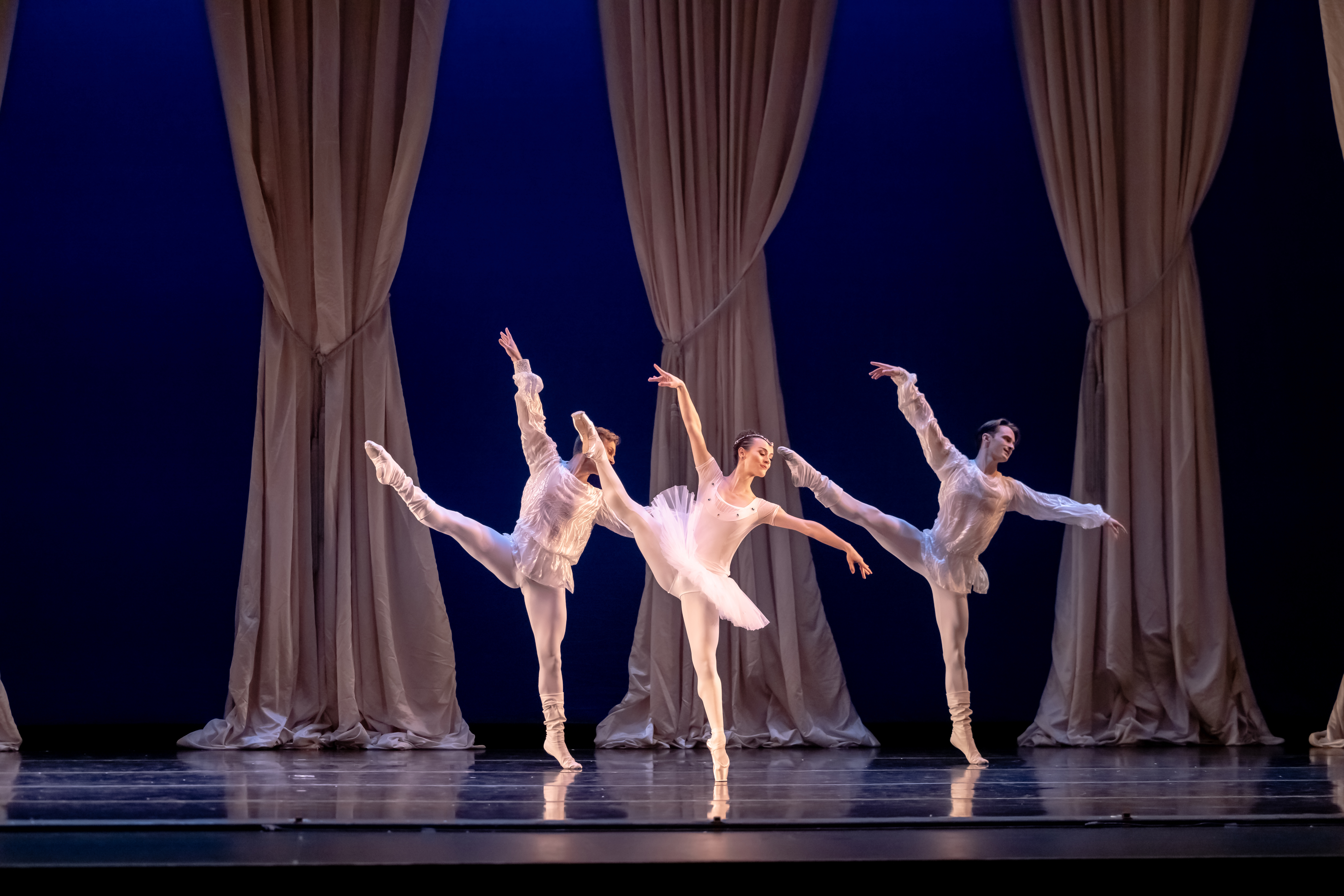 two male dancers and one female on stage extending their leg a la seconde