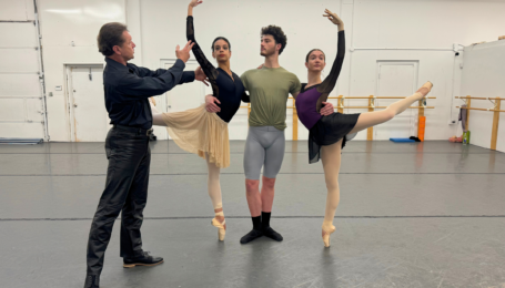 In a dance studio, Timour Bourtasenkov directs a trio of dancers. Gabriela Checo and Breanna Faith Justus pose on either side of Covington Pearson, who supports them as they stand on pointe in attitude derriere.