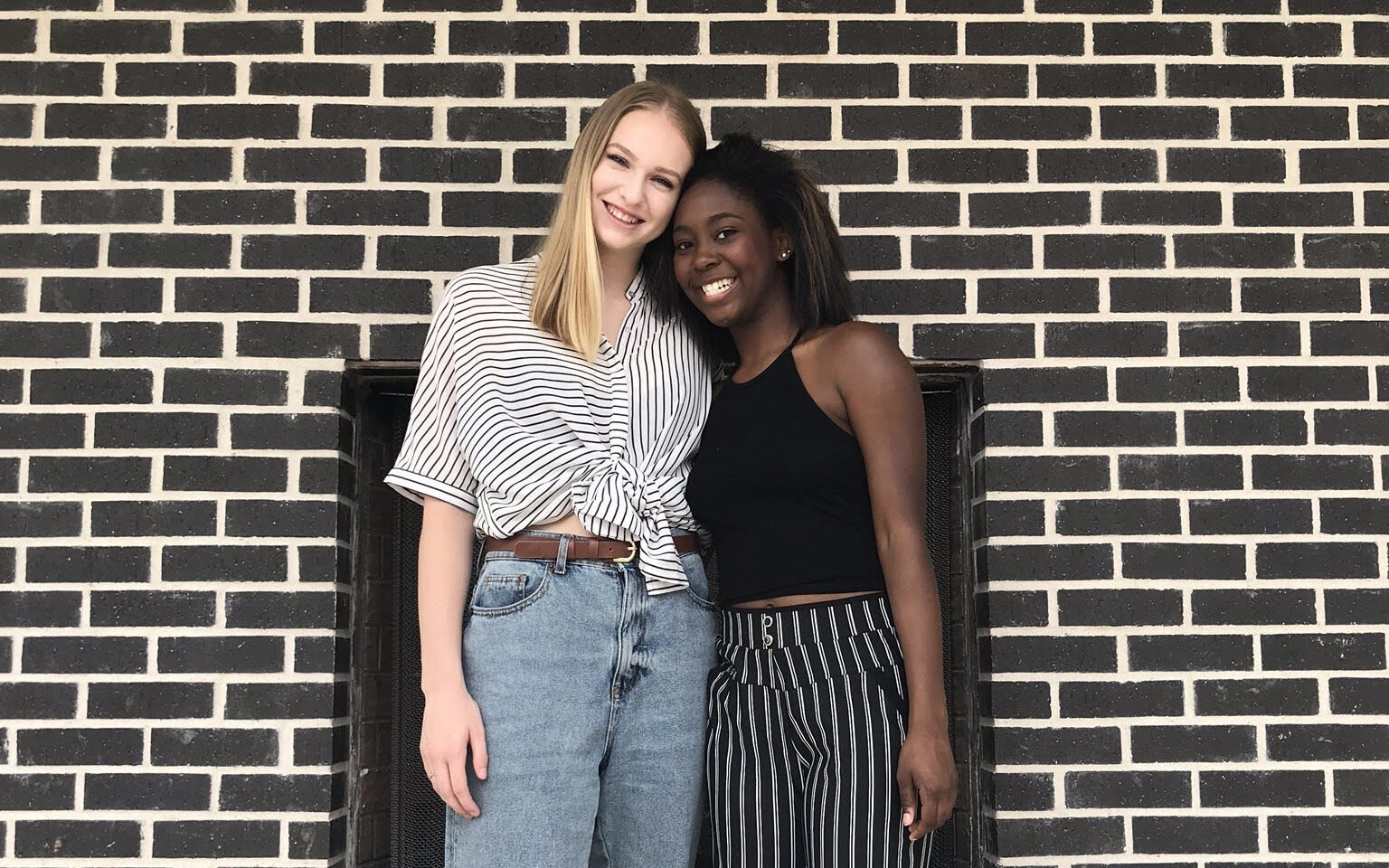 two girls standing close together and smiling at the camera 