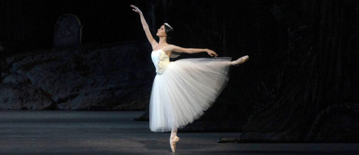 a female dancer wearing a long white tutu performing in first arabesque on stage
