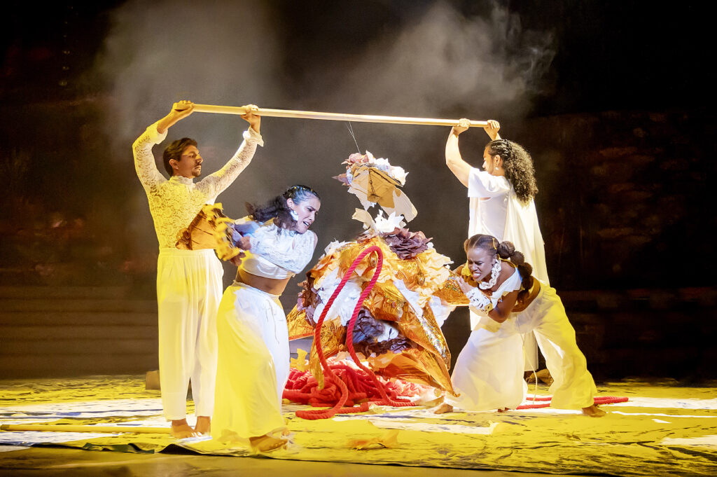 tow dancers holding a pole over their heads with two other dancers moving around them