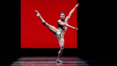 a male dancer wearing short extending his leg a la seconde with his arms going the opposite way