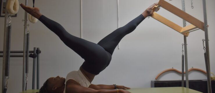 a female dancer on a pilates reformer lifting her hips off the table with her legs in a split